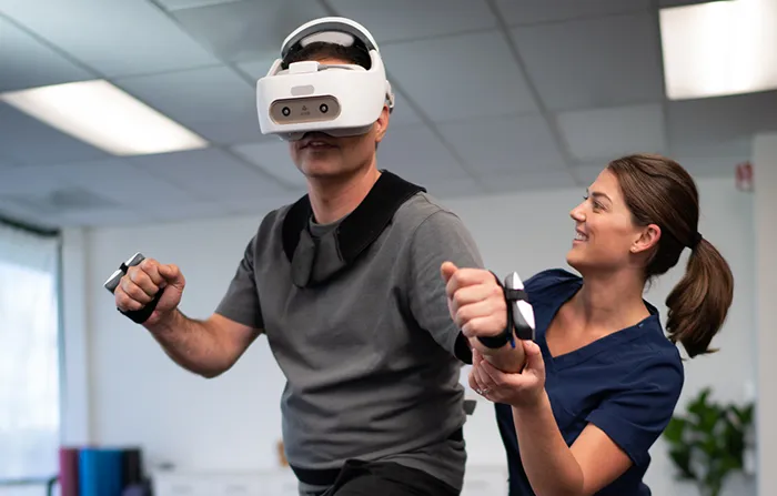 A physical therapist assists a user during rehabilitation with REAL System's VR headset