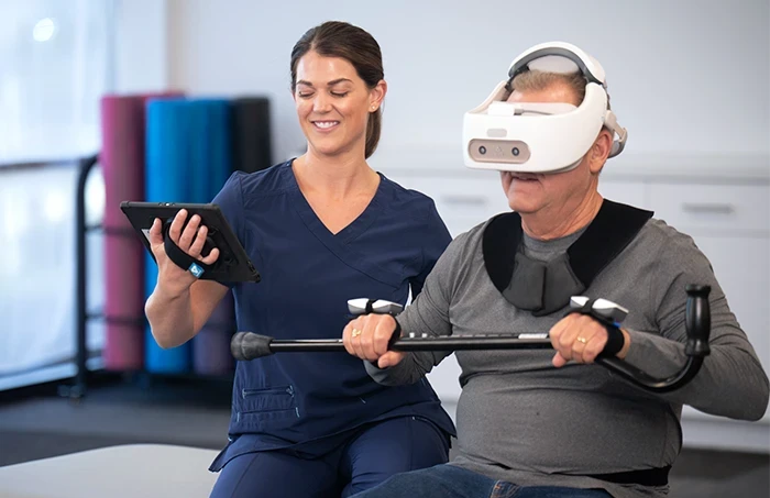 Physical therapist aids user with REAL System headset for upper body rehabilitation