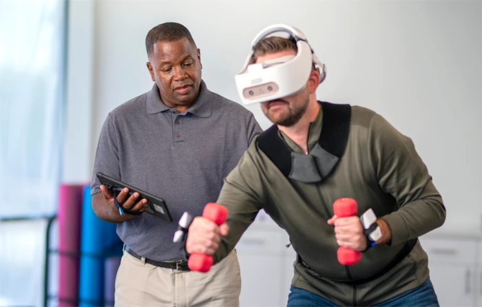 Physical therapist guides a user utilizing REAL System's VR headset for rehabilitation.