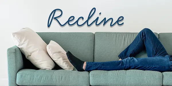 A person lying on a couch with the words "Recline" on the wall behind.