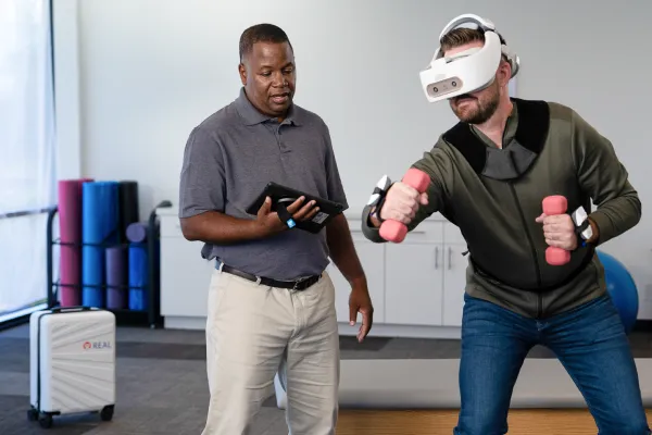 a physical therapist monitors a patient wearing a REAL y-Series VR rehabilitation device